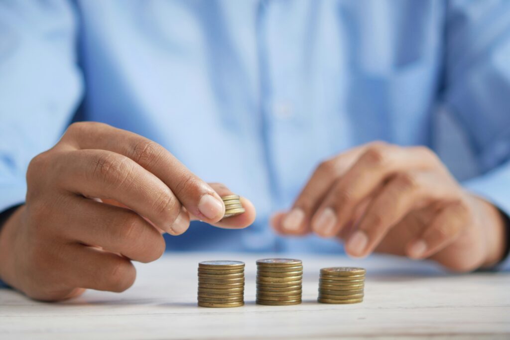 Close-up of a person in a blue shirt stacking coins into small piles on a table, representing saving or budgeting money.