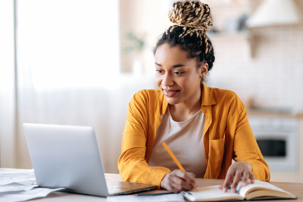 6 Practical Financial Habits to Focus on This Year Woman using a laptop and writing in a notebook at a table.