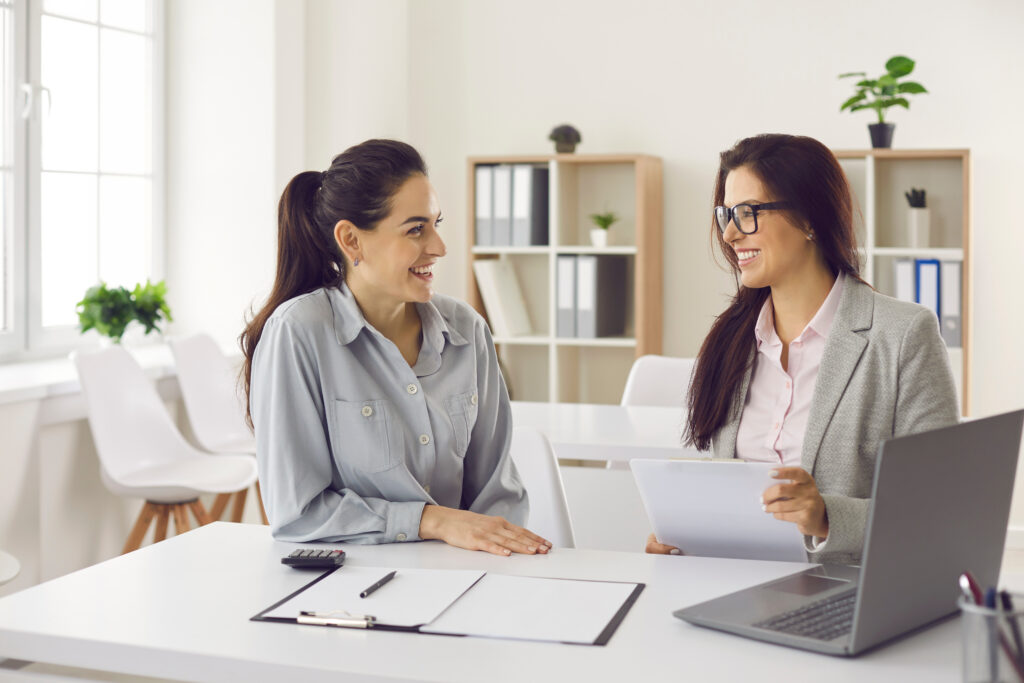Closed-End Credit Definition and Examples Two women sitting at a desk in an office, smiling and reviewing documents together.