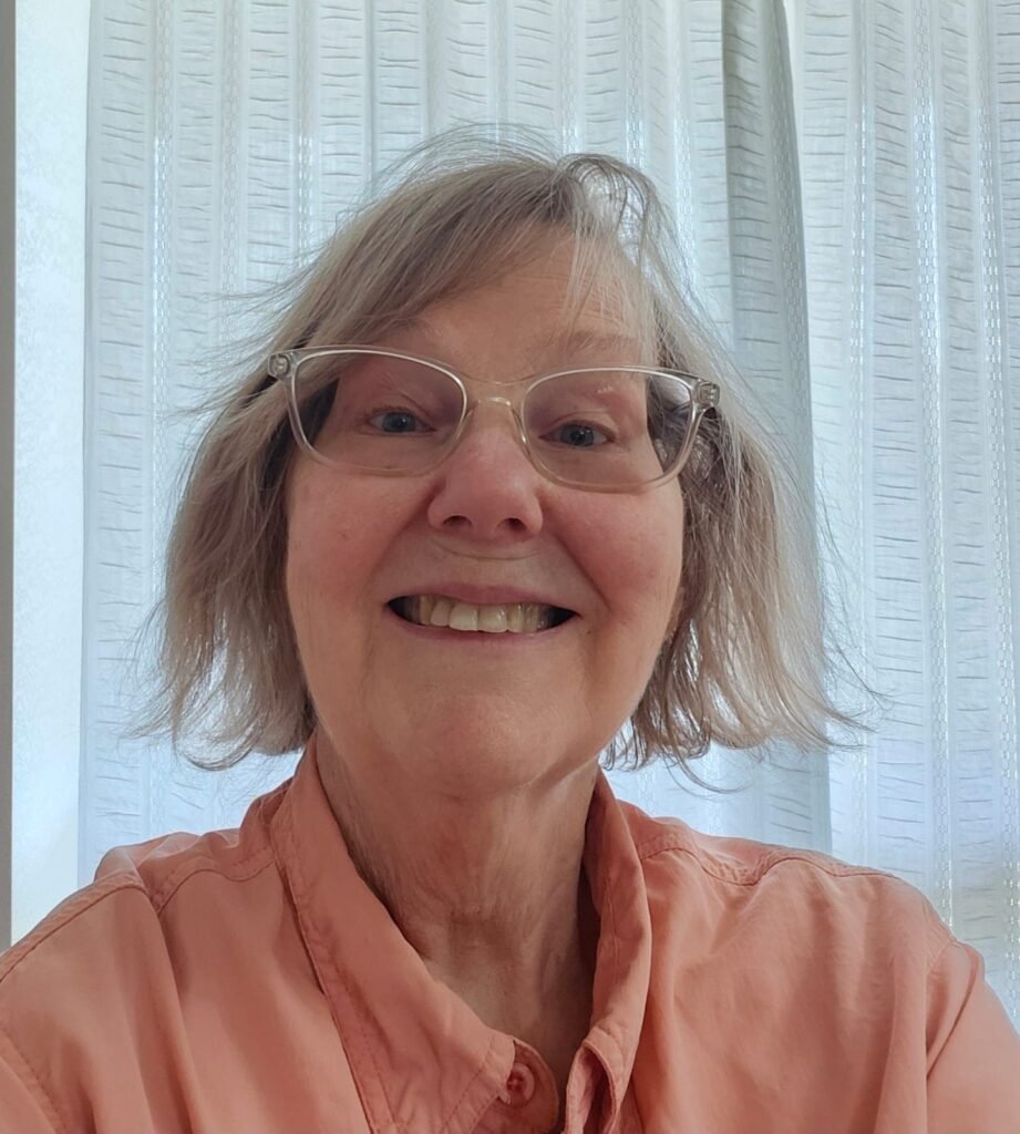Close-up of a smiling older woman wearing glasses and a button-up shirt indoors