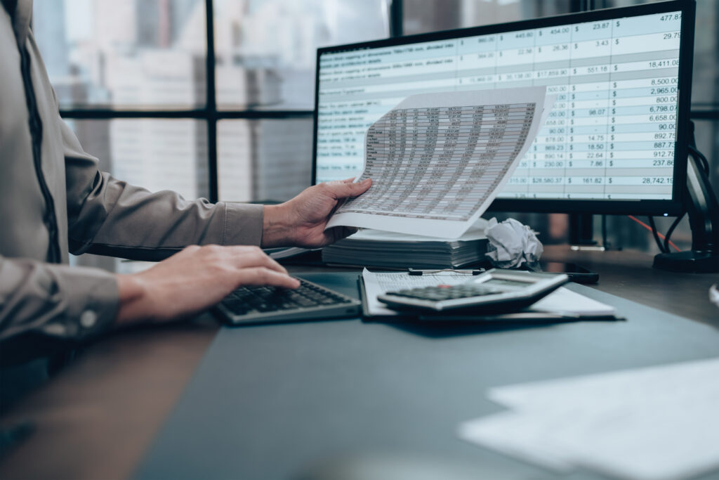 What Is a Loan Prepayment Penalty? Person reviewing financial documents while using a calculator and computer with spreadsheet data on screen