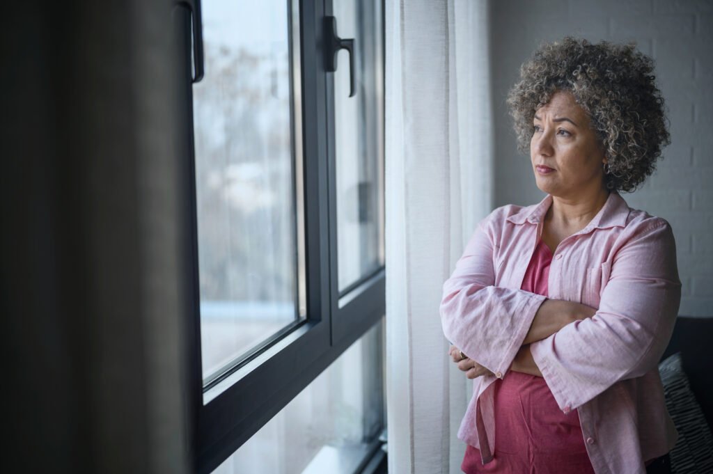 Do Evictions Show Up on Your Credit Report Woman standing by a window with her arms crossed, looking outside thoughtfully.