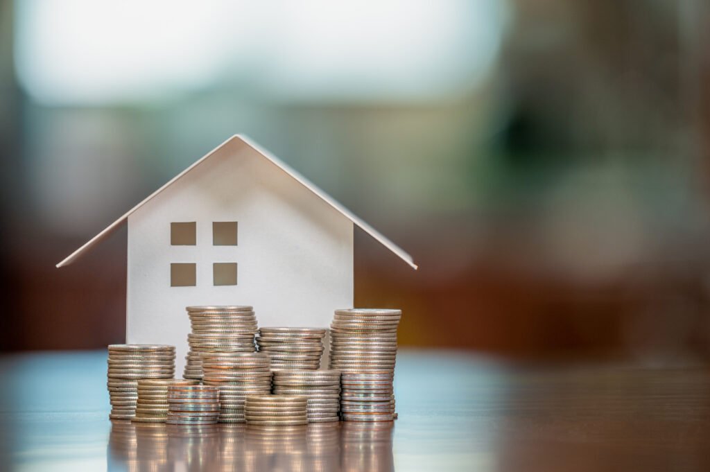 Grace Period for Mortgage Payment Explained Paper house model surrounded by stacks of coins on a table, representing homeownership, savings, or mortgage planning.