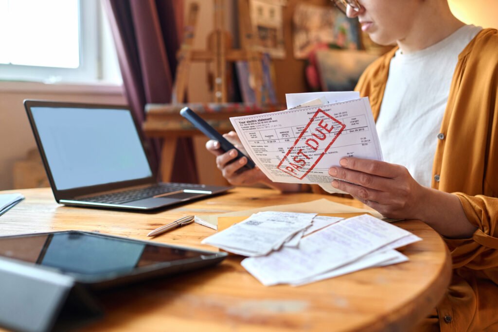What Happens When a Bill Goes to Collections? Woman reviewing an overdue bill while holding a smartphone at a table with a laptop and receipts.