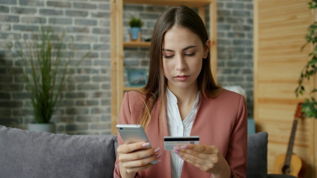 Young woman holding credit card and smartphone; credit card debt