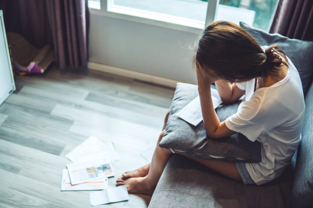 Debt and Mental Health: Breaking the Stress Cycle Stressed woman sitting on a couch with bills and paperwork scattered nearby.