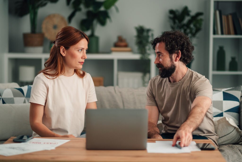 How to Cancel a Timeshare: Legal Steps and Costs Couple sitting on a sofa with a laptop and papers, talking to each other.